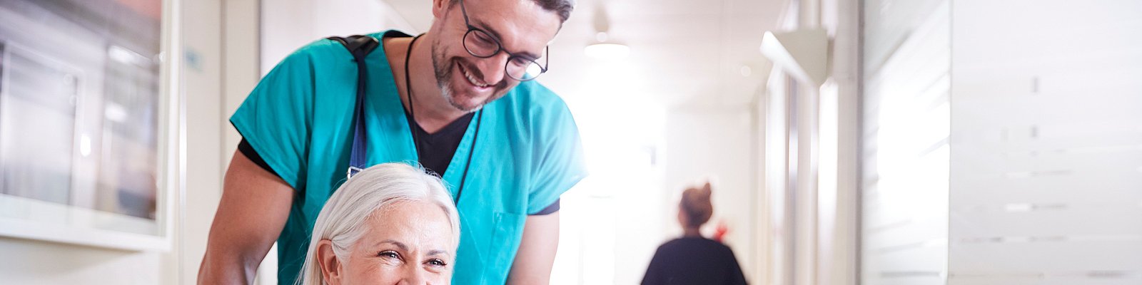 Pflegeassistent schiebt Frau im Rollstuhl